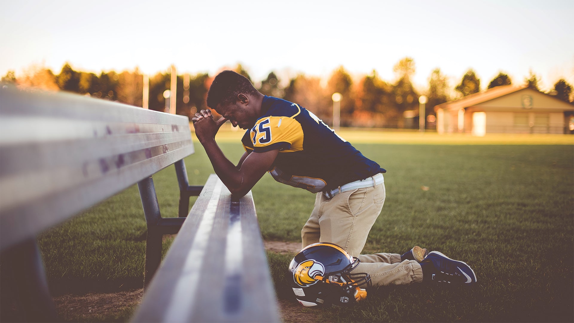 American Football speler knielt en bidt bij een bankje.