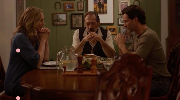 The family sits together at the table in prayer, a quiet moment of connection amid the tensions within the household.